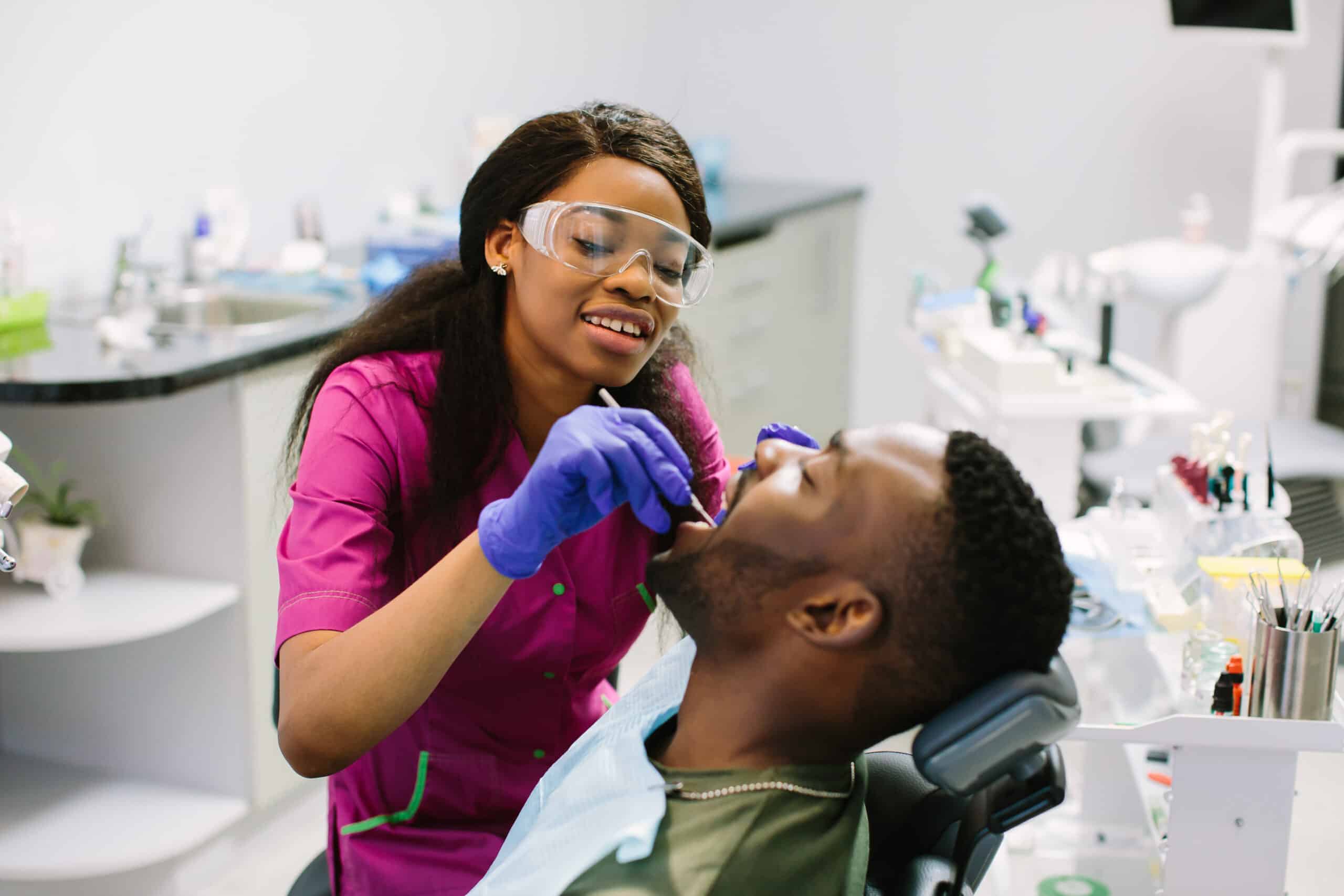 Young african american man lying in chair receiving dental treatment with mouth open, dentist hands wearing gloves holding tools working on patients teeth